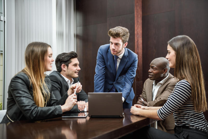 Business meeting with 5 people sitting at table with a laptop.